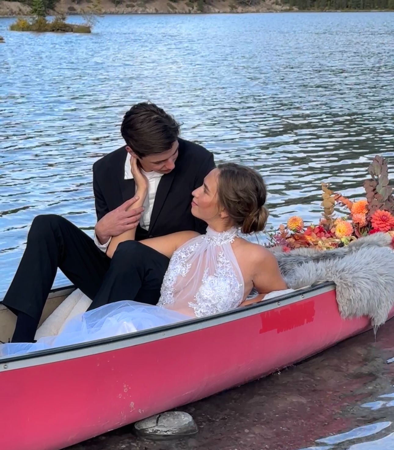 Couple relaxes in red canoe decorated with flowers on serene lake.