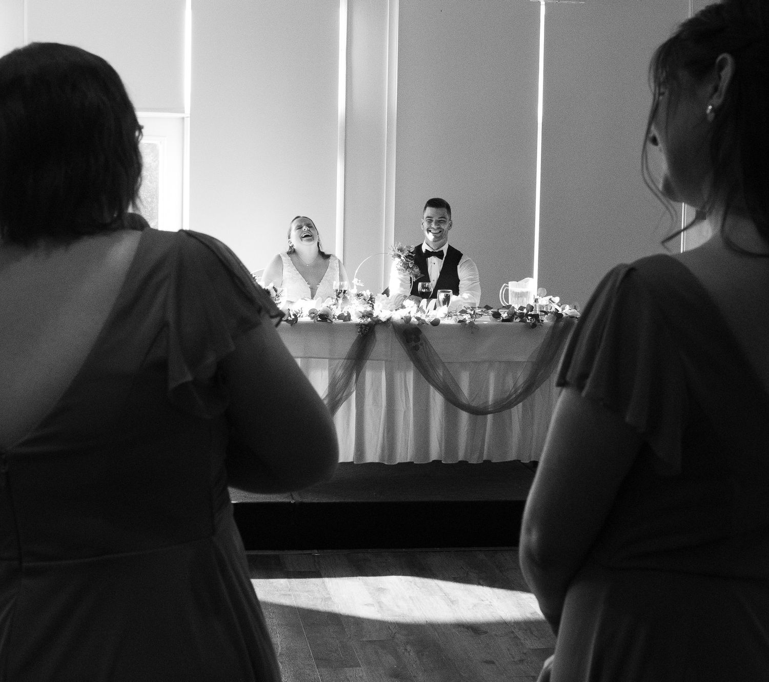 Black and white photo showing wedding guests watching a couple dance during their first dance at a reception.