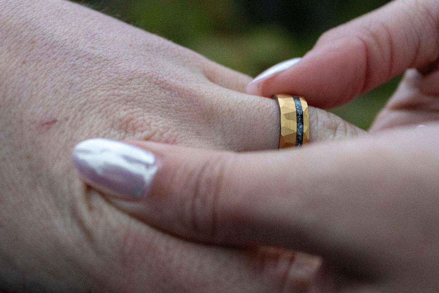 Close-up of hands adjusting a wedding ring with white manicured nails.