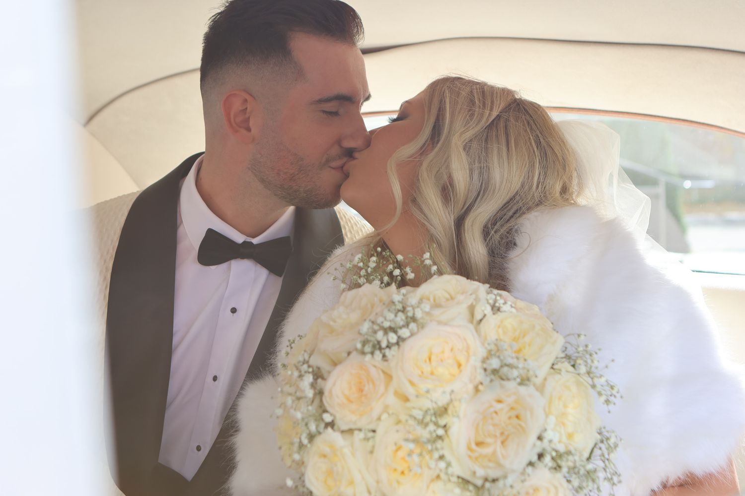 A romantic wedding moment in a car with a beautiful white and cream rose bouquet.