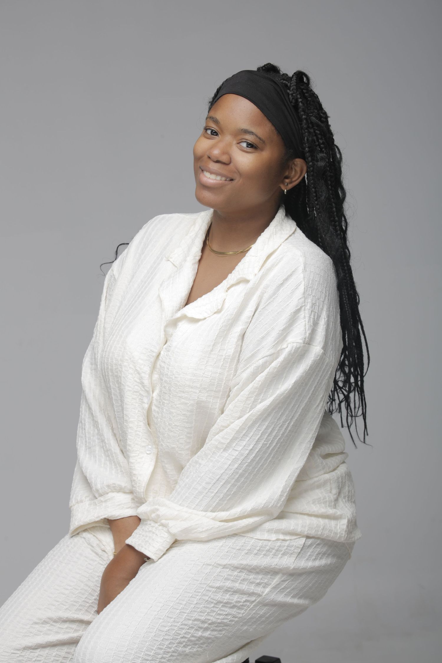 Portrait of woman in white textured robe and black headband with long braids against gray background.