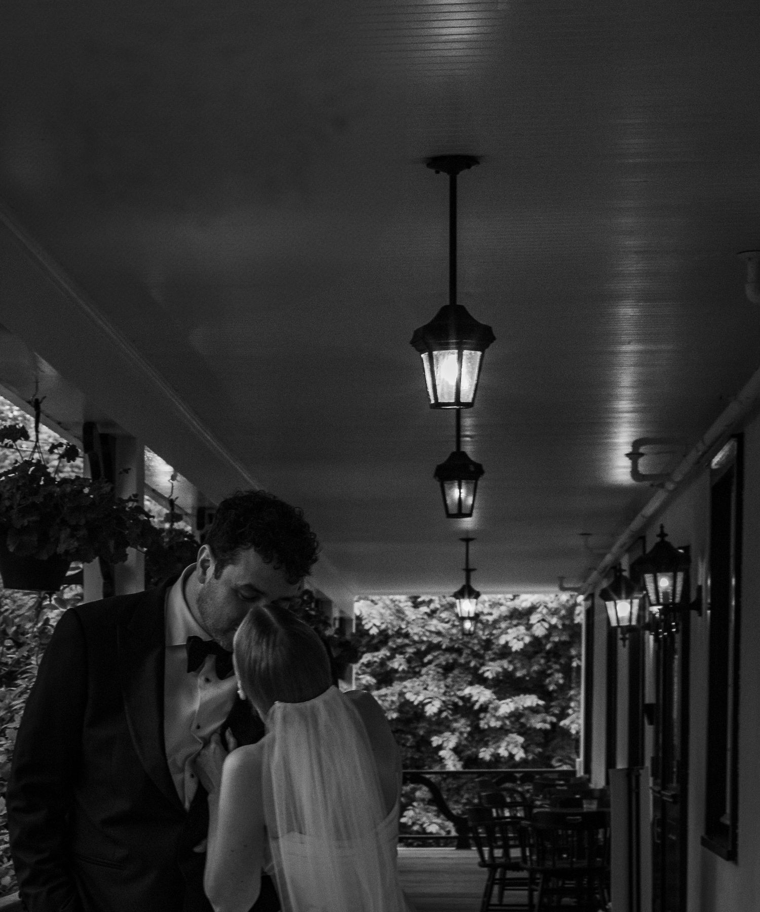 A romantic black and white wedding moment captured on a porch with hanging lanterns creating an intimate atmosphere.