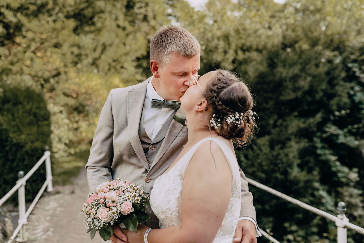 A couple shares an intimate moment on their wedding day outdoors with baby's breath bouquet and grey suit attire.