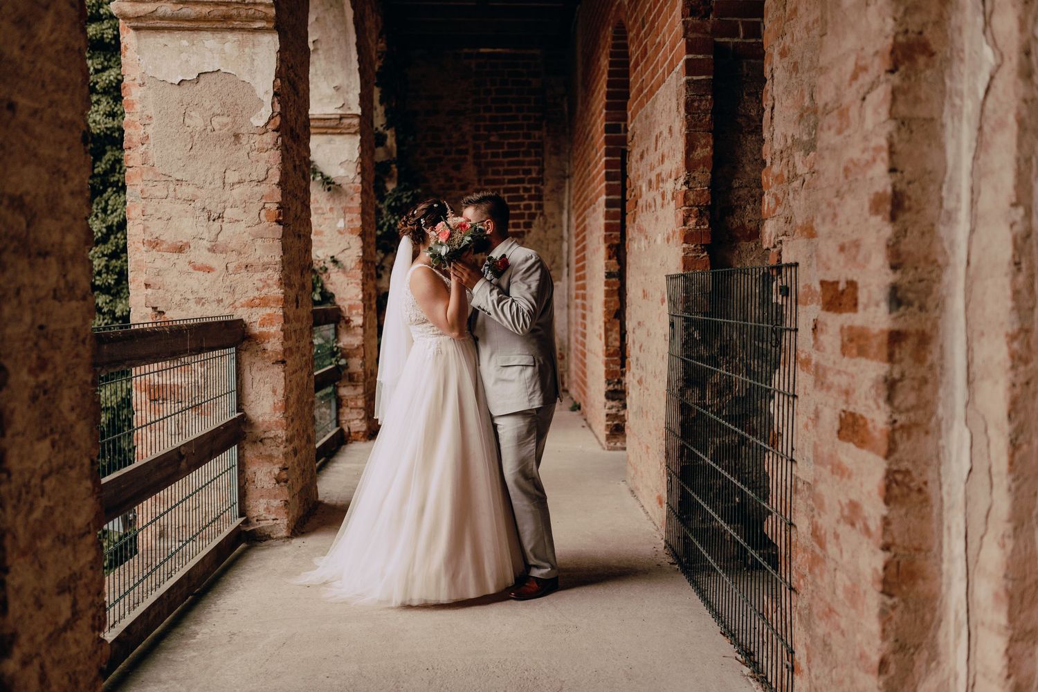A wedding couple embracing in an elegant brick archway corridor.