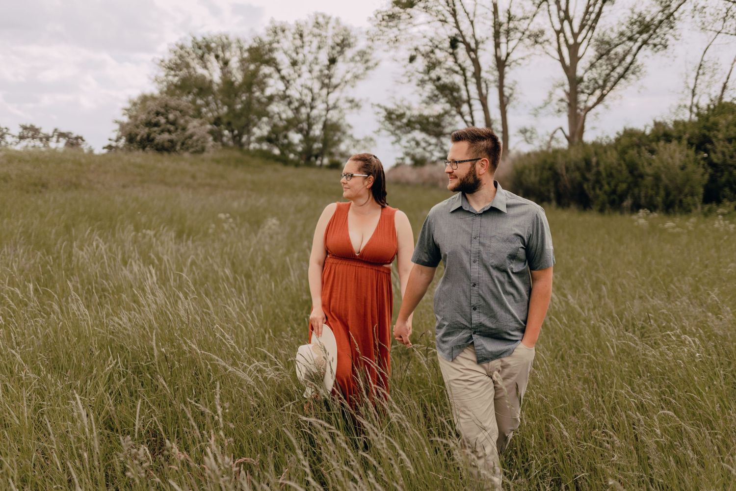 Couple in casual attire walking together through a scenic meadow field on an overcast day.