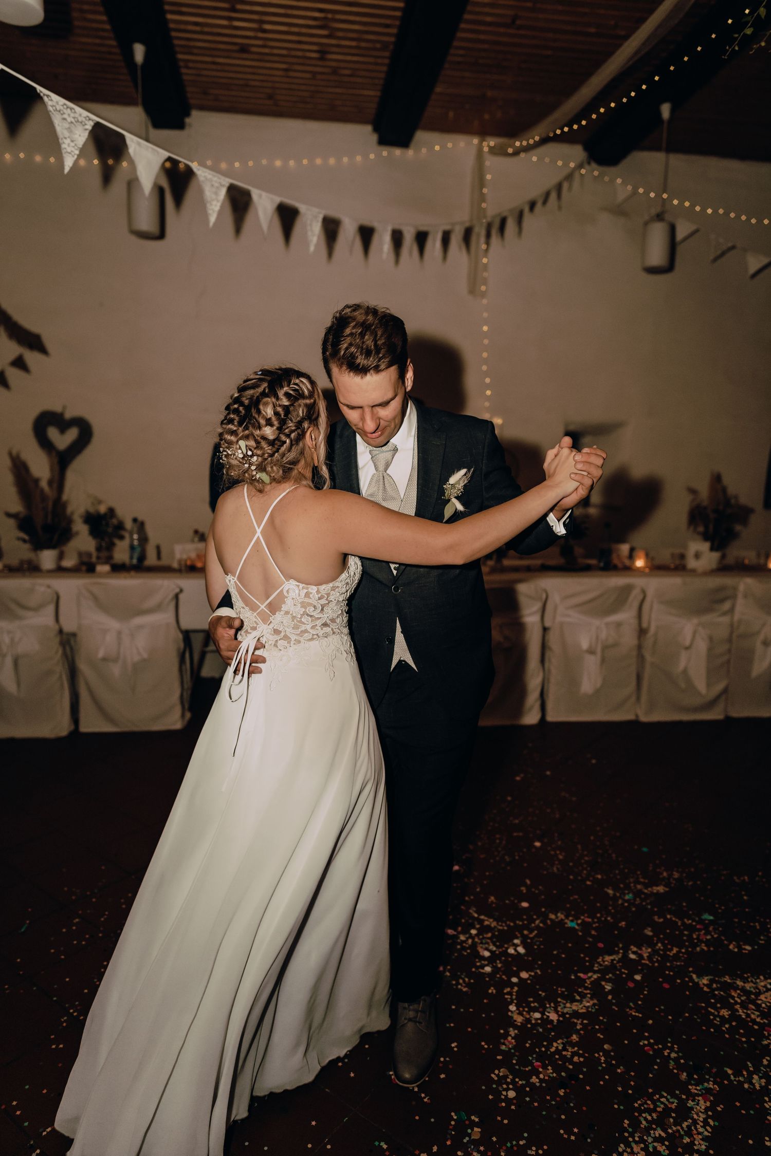 Newlywed couple dancing together at their wedding reception under decorative bunting and string lights.