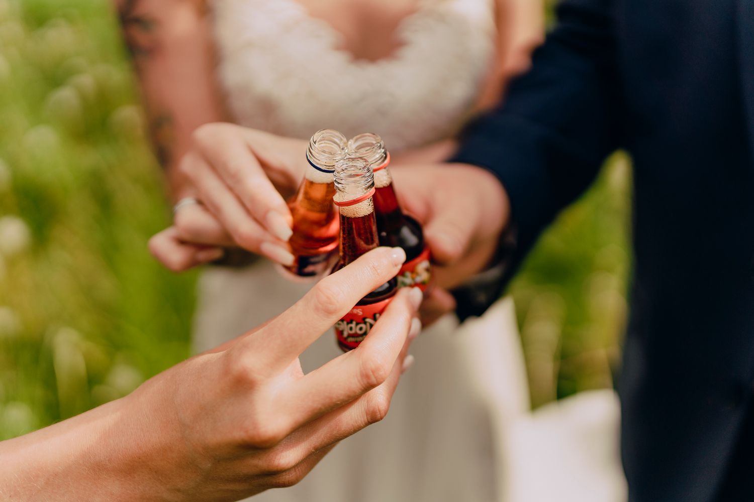 Hands reaching for small bottles of red alcohol at an outdoor event or celebration.