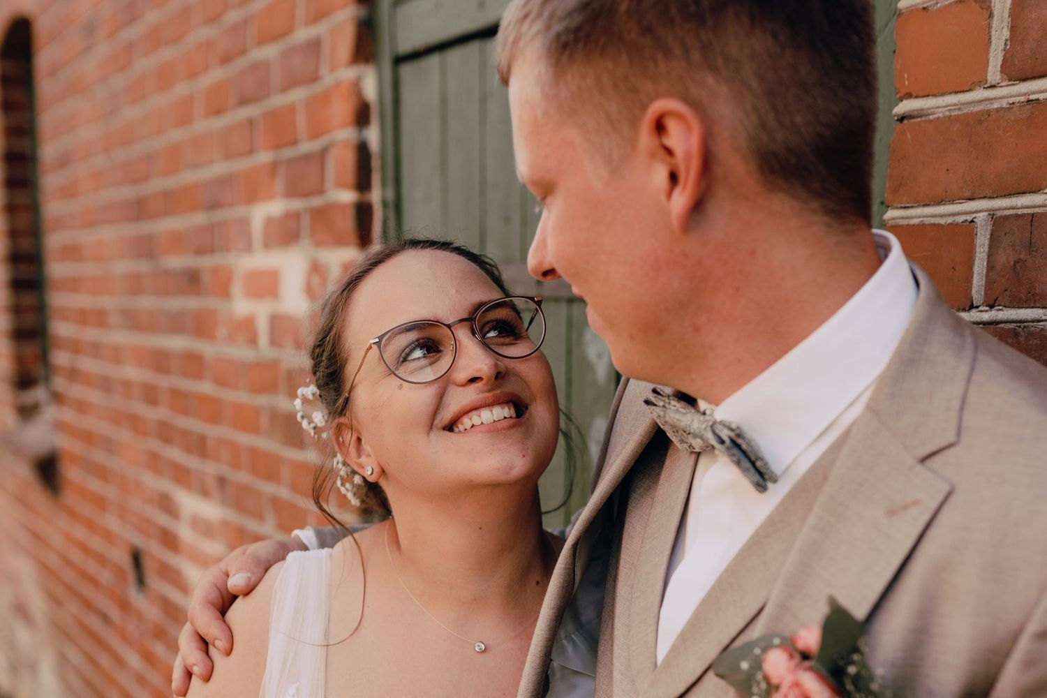 A happy couple shares a romantic moment together against a rustic brick wall backdrop.