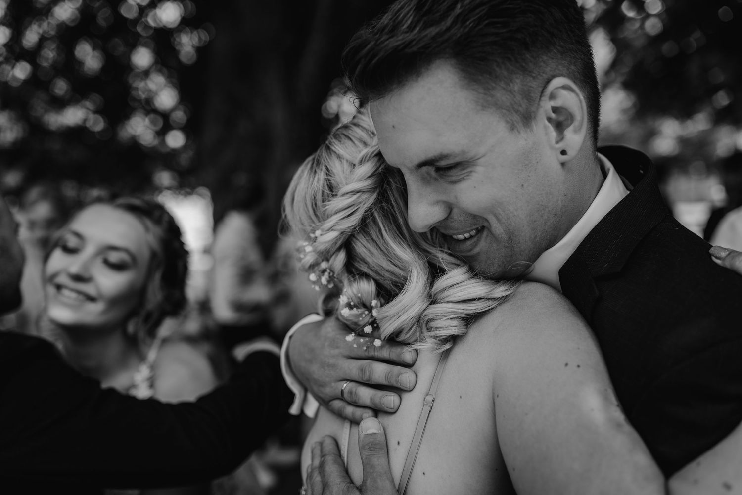 Black and white photograph showing an intimate emotional embrace during an outdoor wedding celebration.