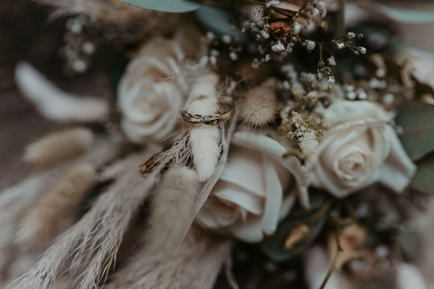 Close-up detail of soft pink roses and delicate dried pampas grass in a moody wedding bouquet arrangement.