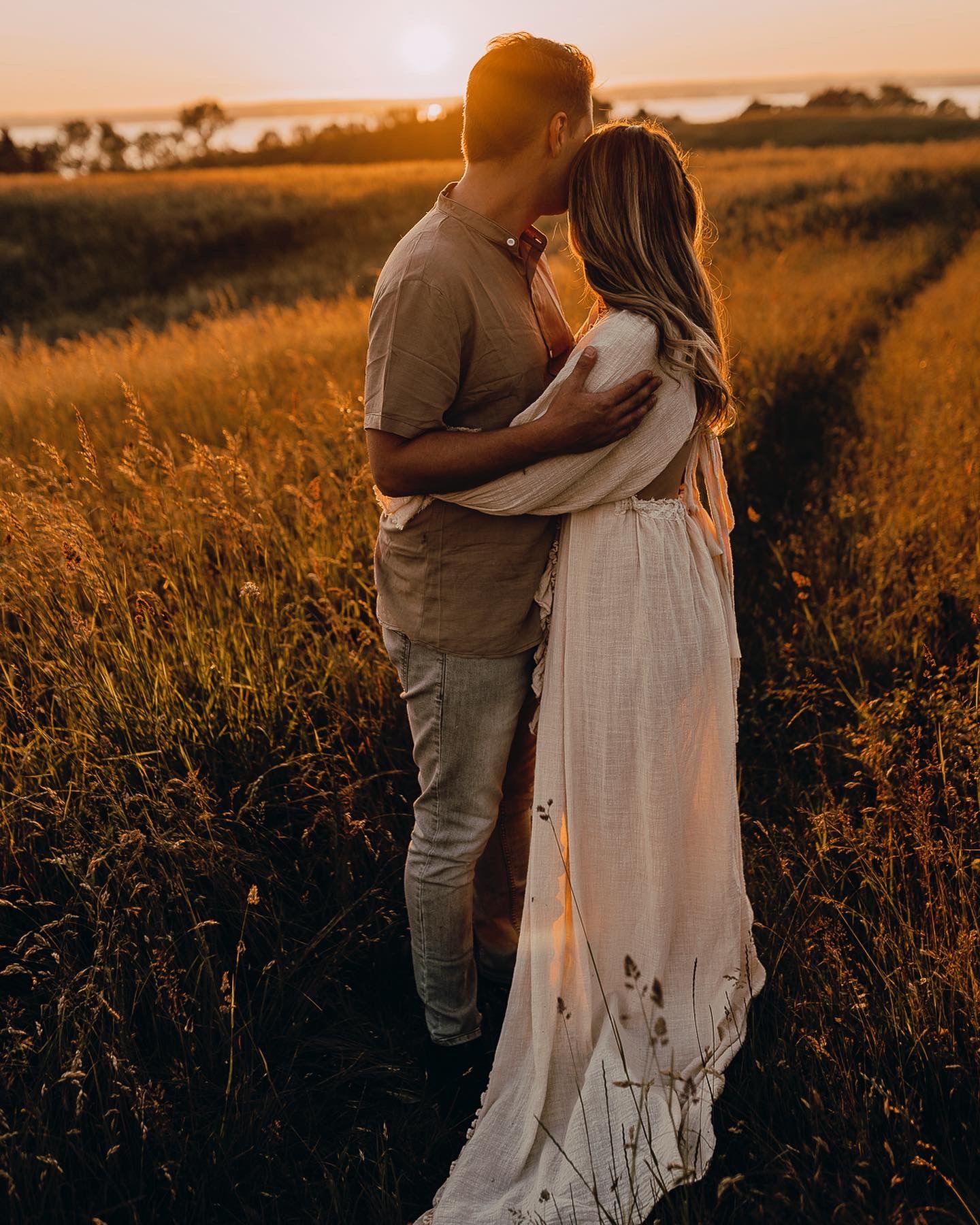 A couple embraces in a golden field at sunset creating a romantic silhouette against the warm summer evening light.