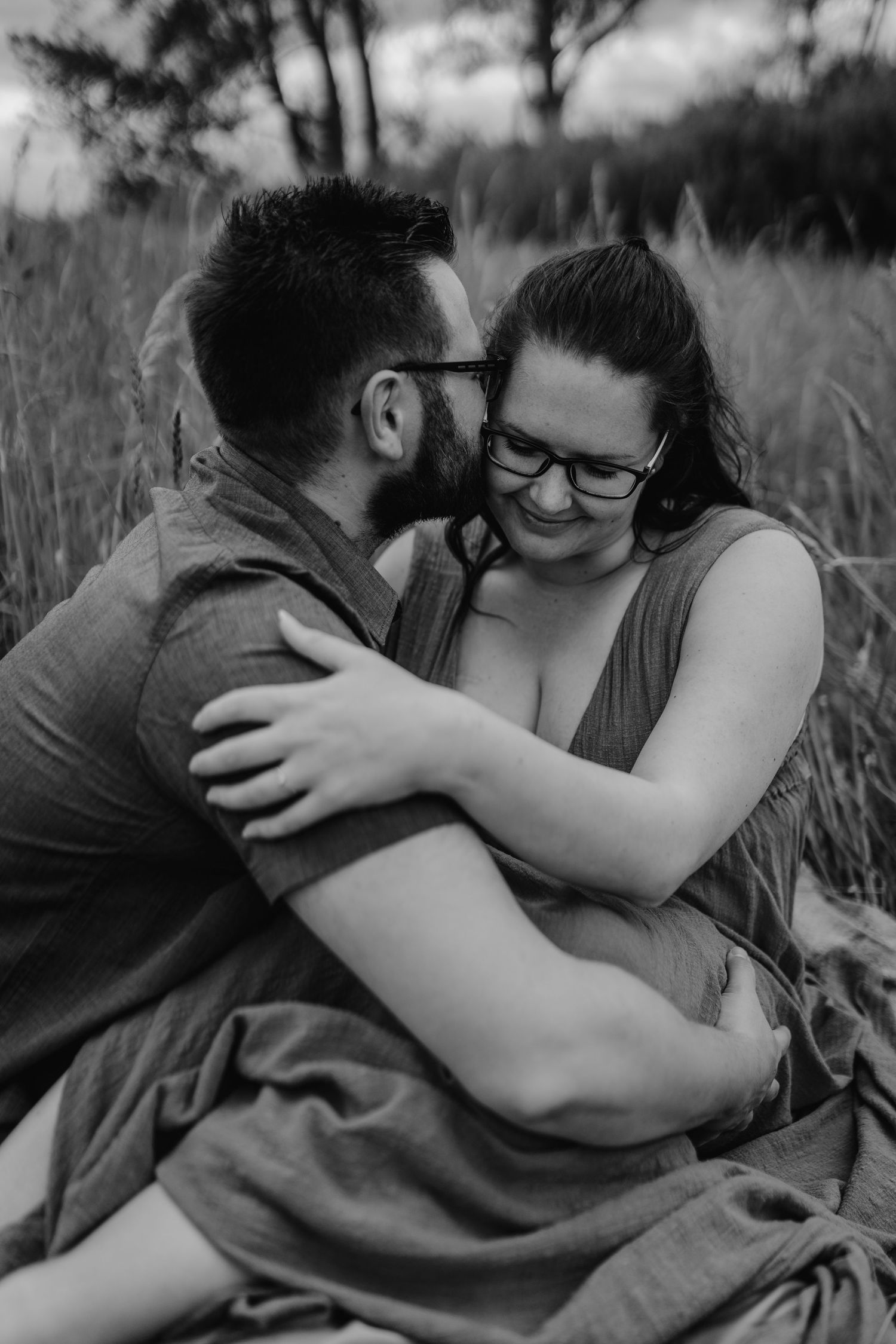 Intimate black and white portrait of couple sharing tender moment among tall grass in field.