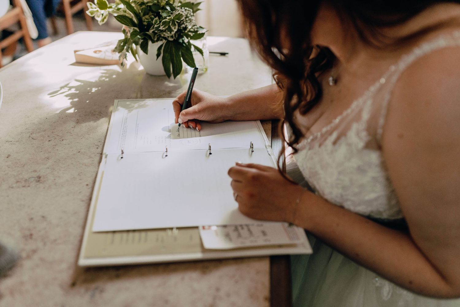 Someone signing a document with a small floral arrangement on the table.