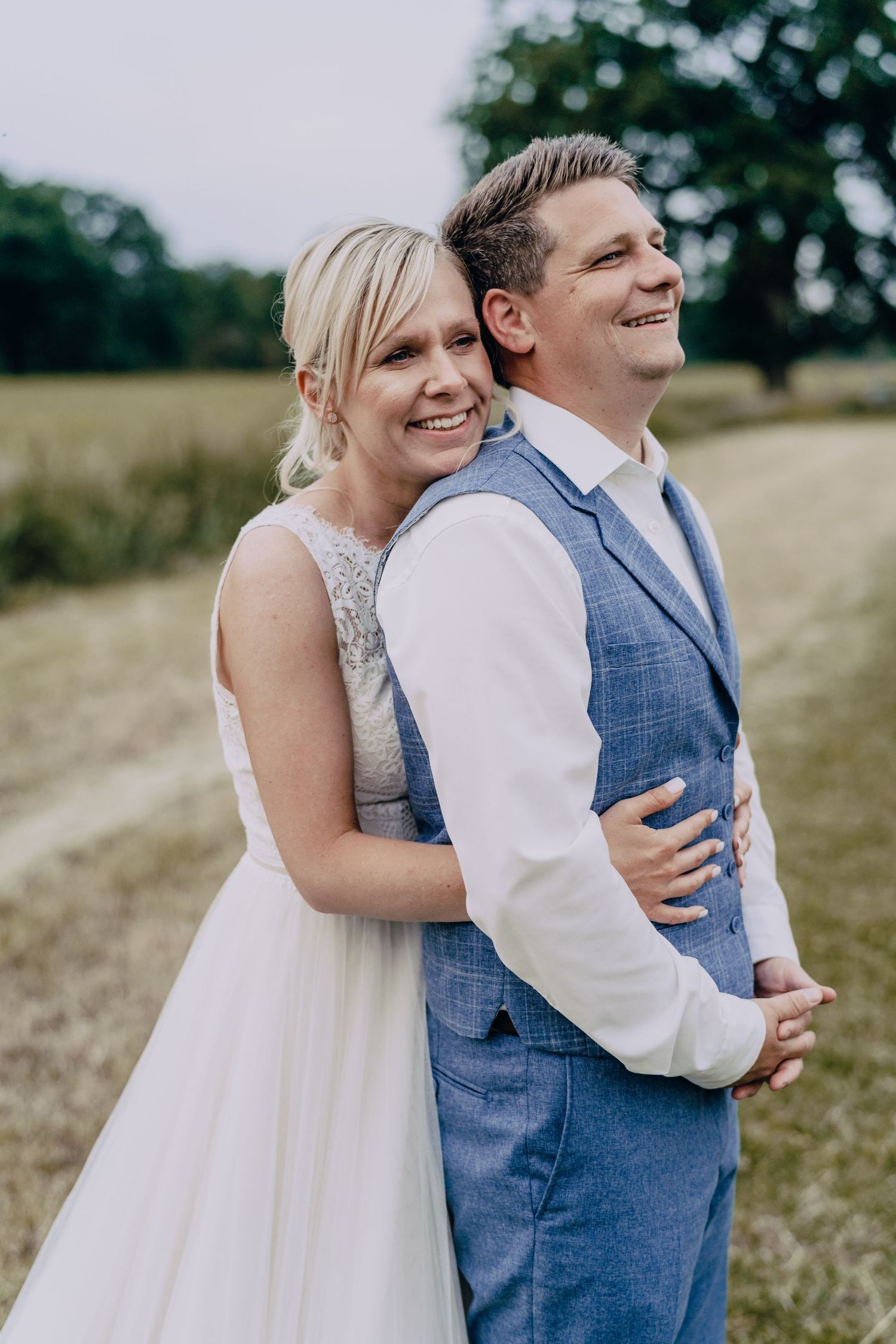 A couple embraces in an outdoor field wearing wedding attire while laughing and enjoying the moment.