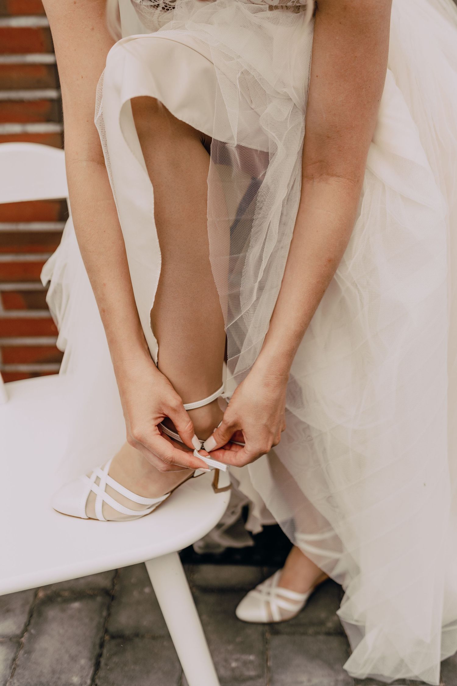 Close-up shots of a bride putting on elegant white wedding shoes with tulle dress in view.