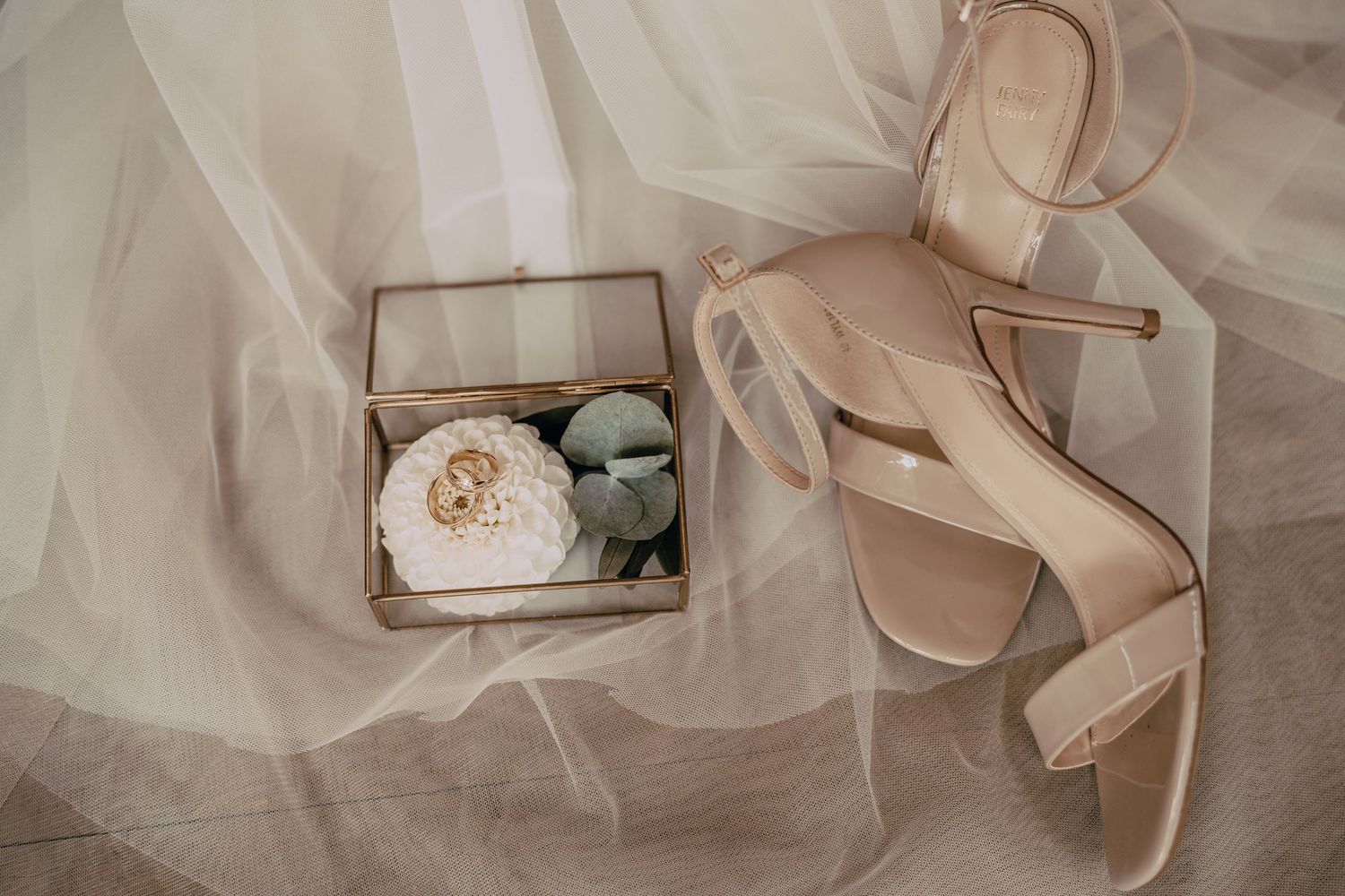 Delicate tulle fabric and blush pink bridal shoes arranged with wedding accessories in soft natural light.