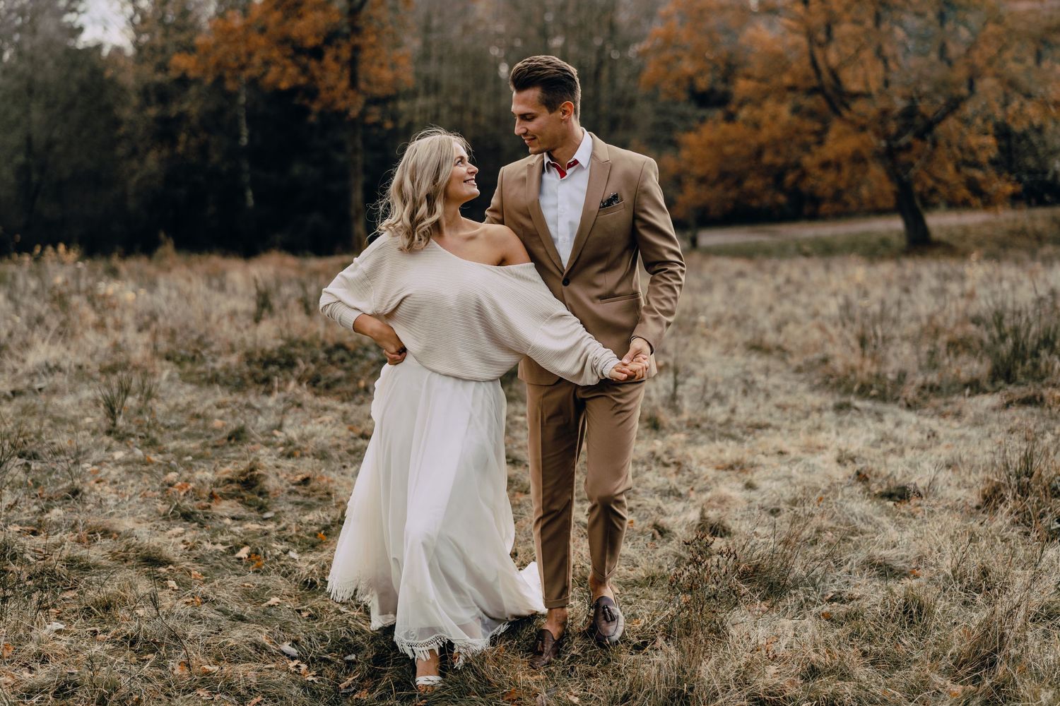 A couple shares a romantic moment in a rustic autumn field while wearing elegant wedding attire.