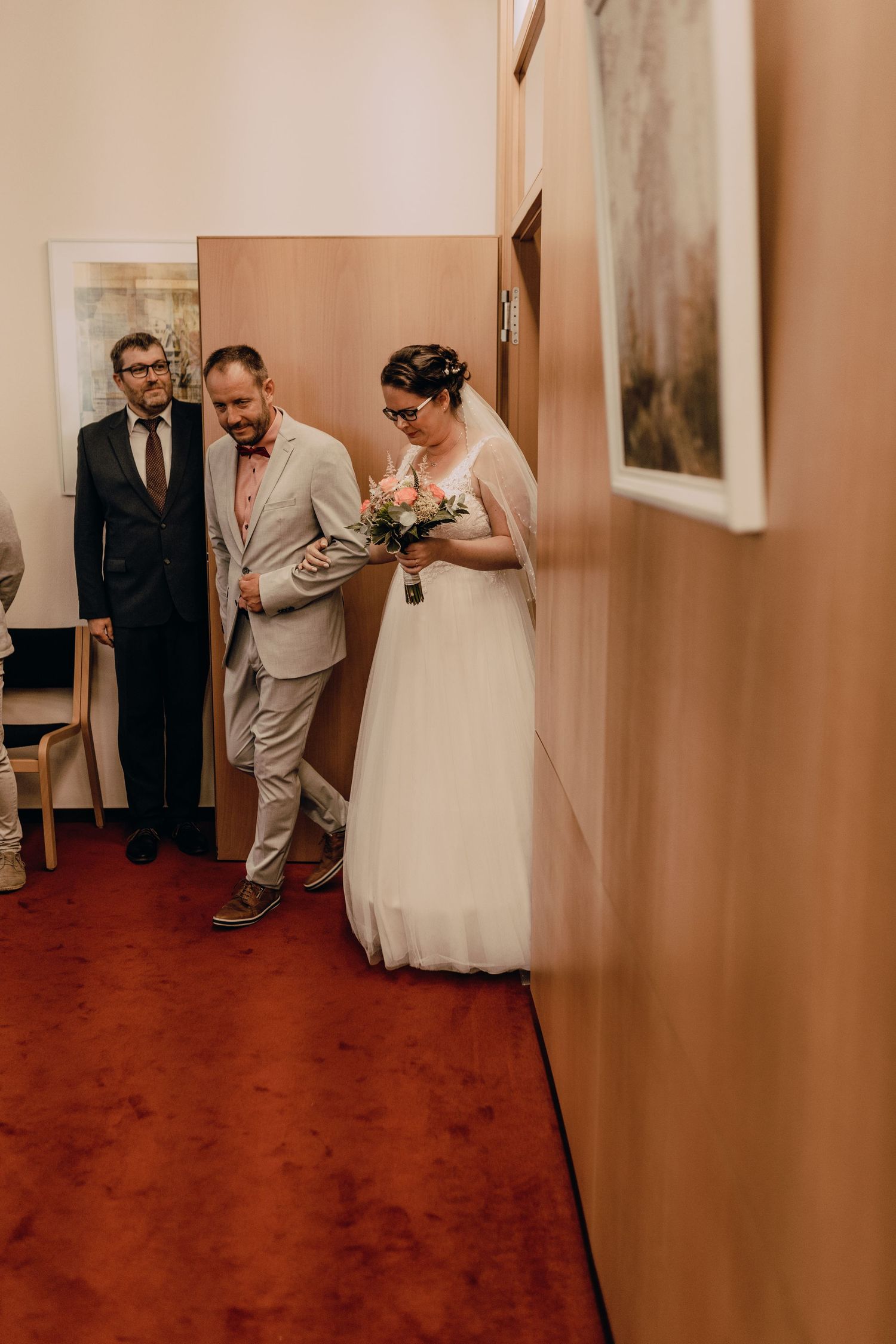 Wedding ceremony participants walking down a hallway with red flooring.