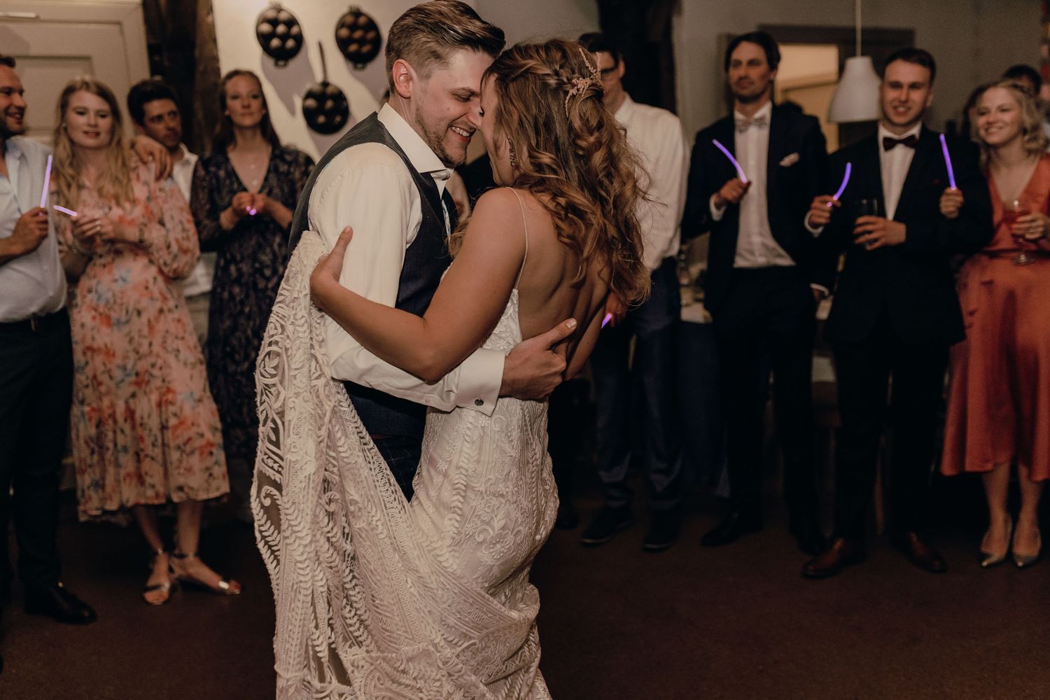 Wedding couple sharing their first dance surrounded by guests in a dimly lit reception venue.