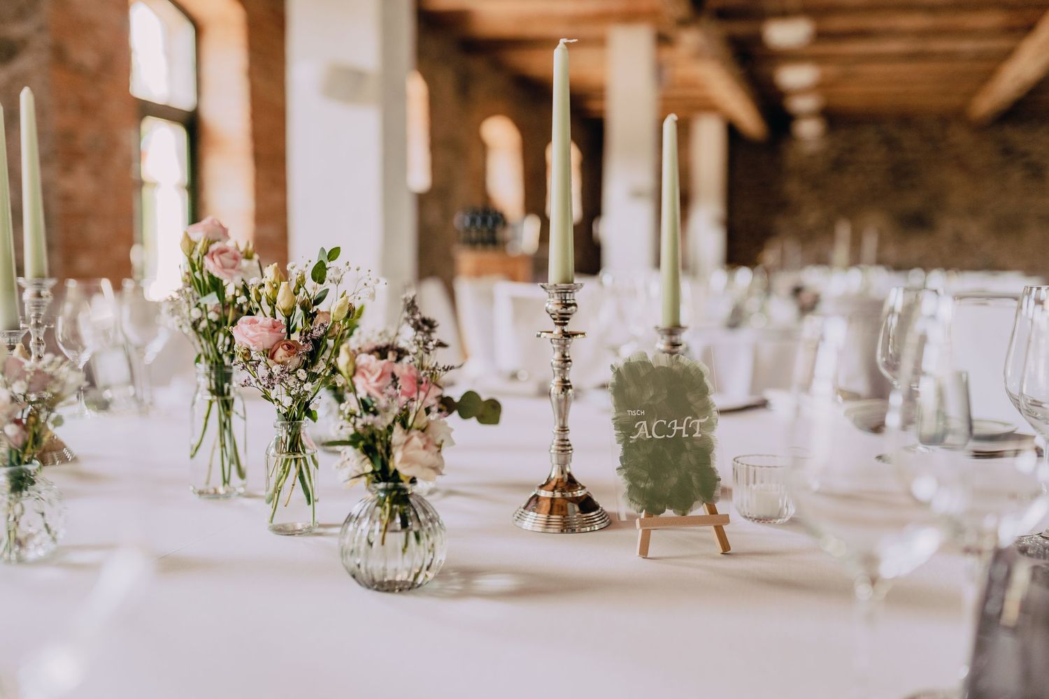 Elegant table setting with delicate flower arrangements in glass vases and tall white candles.