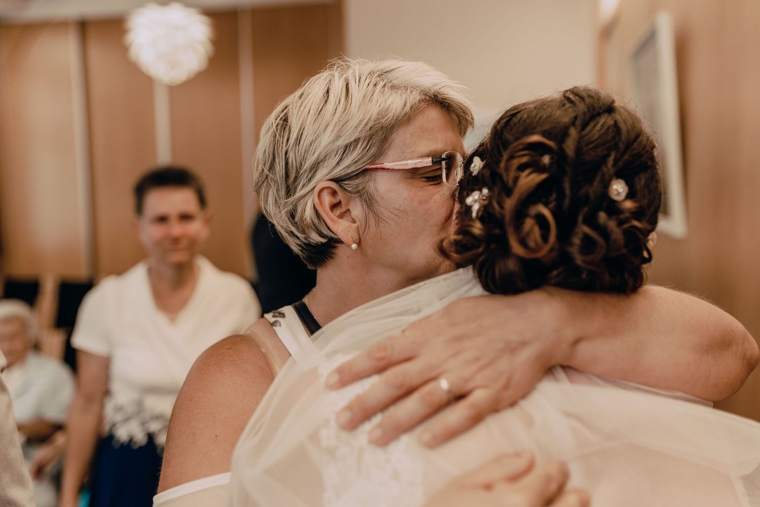 Emotional moment at a wedding celebration with guests embracing in a reception hall.