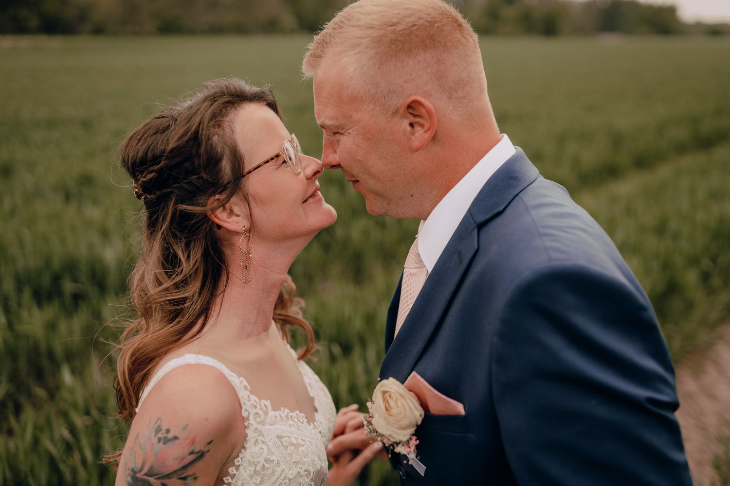 Joyful couple in wedding attire share intimate moments in a lush green field during golden hour.