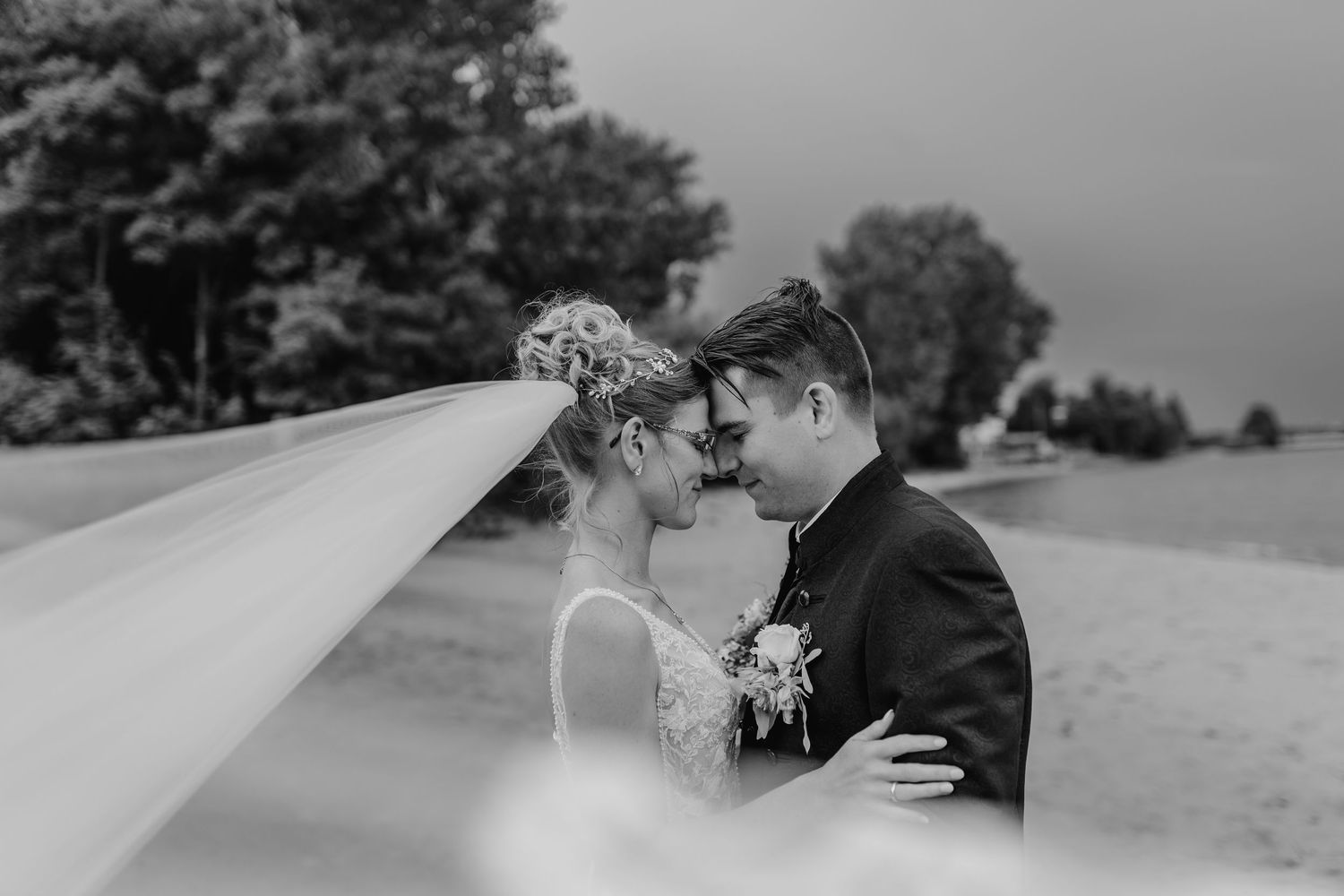 A romantic black and white wedding photograph captures an intimate moment between a couple outdoors.