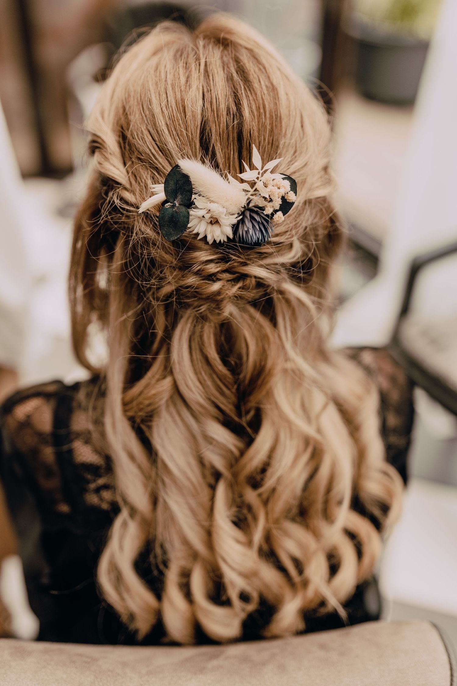 Elegant bridal hairstyle featuring soft blonde waves and delicate floral hair accessories in black and cream tones.