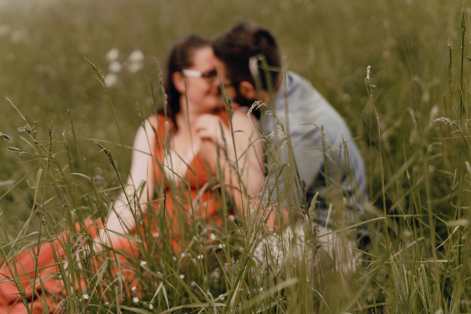 Photographer and subject sitting together in tall grass during golden hour photo session.