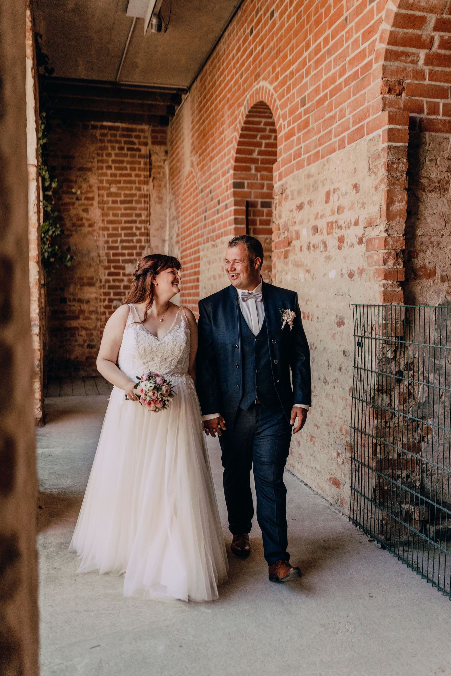 Wedding couple walking together through a rustic brick corridor with exposed walls and soft natural lighting.