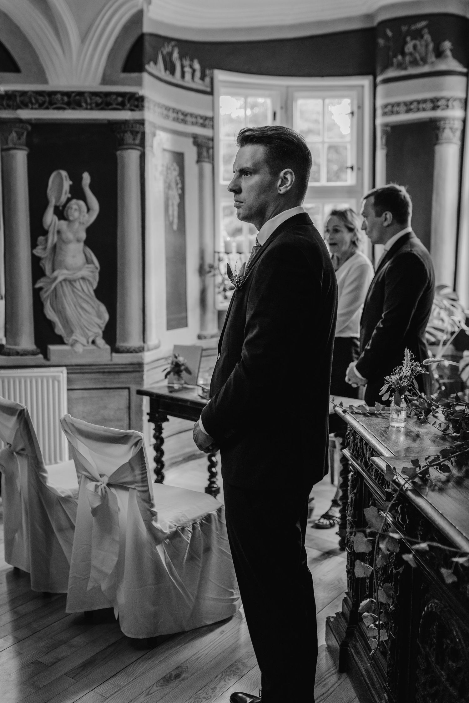 An elegant wedding ceremony in a grand room with ornate architectural details and classical statues.
