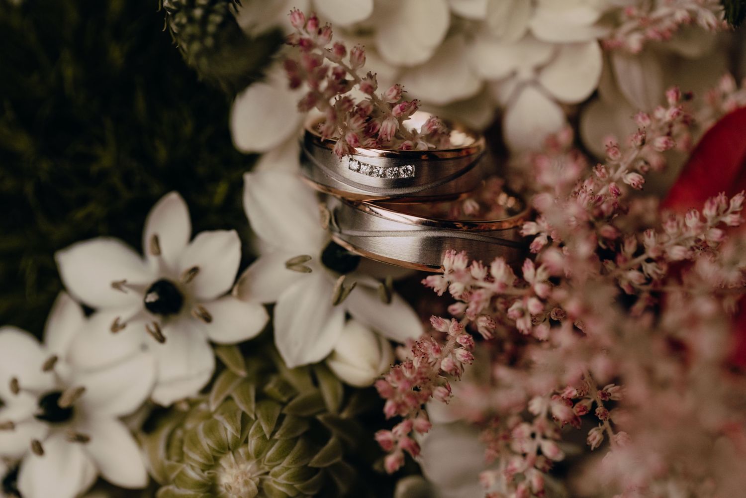 Wedding rings displayed among soft pink and white floral arrangements.