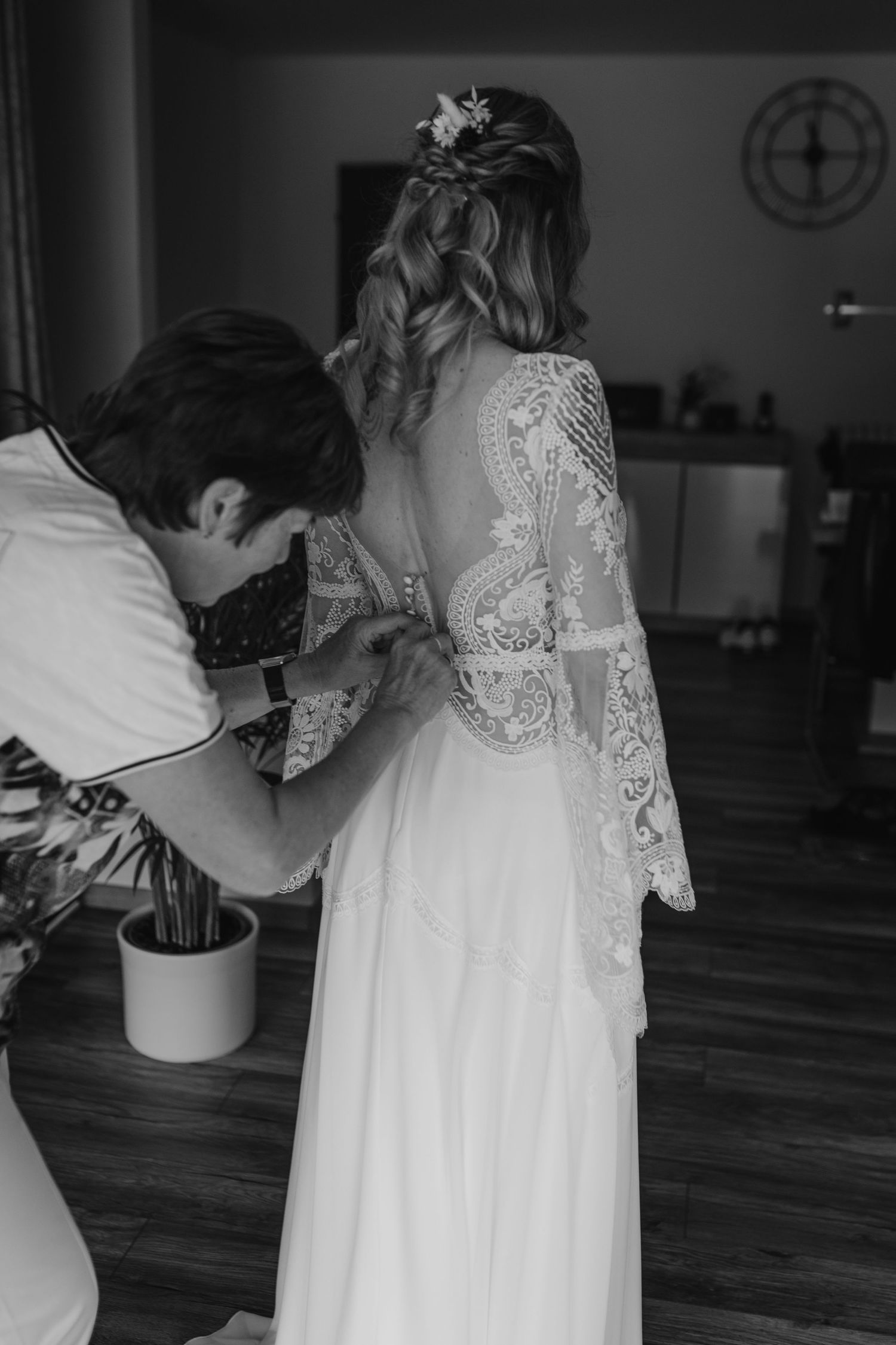 Close-up black and white photo of a delicate lace wedding dress with long sleeves being adjusted.