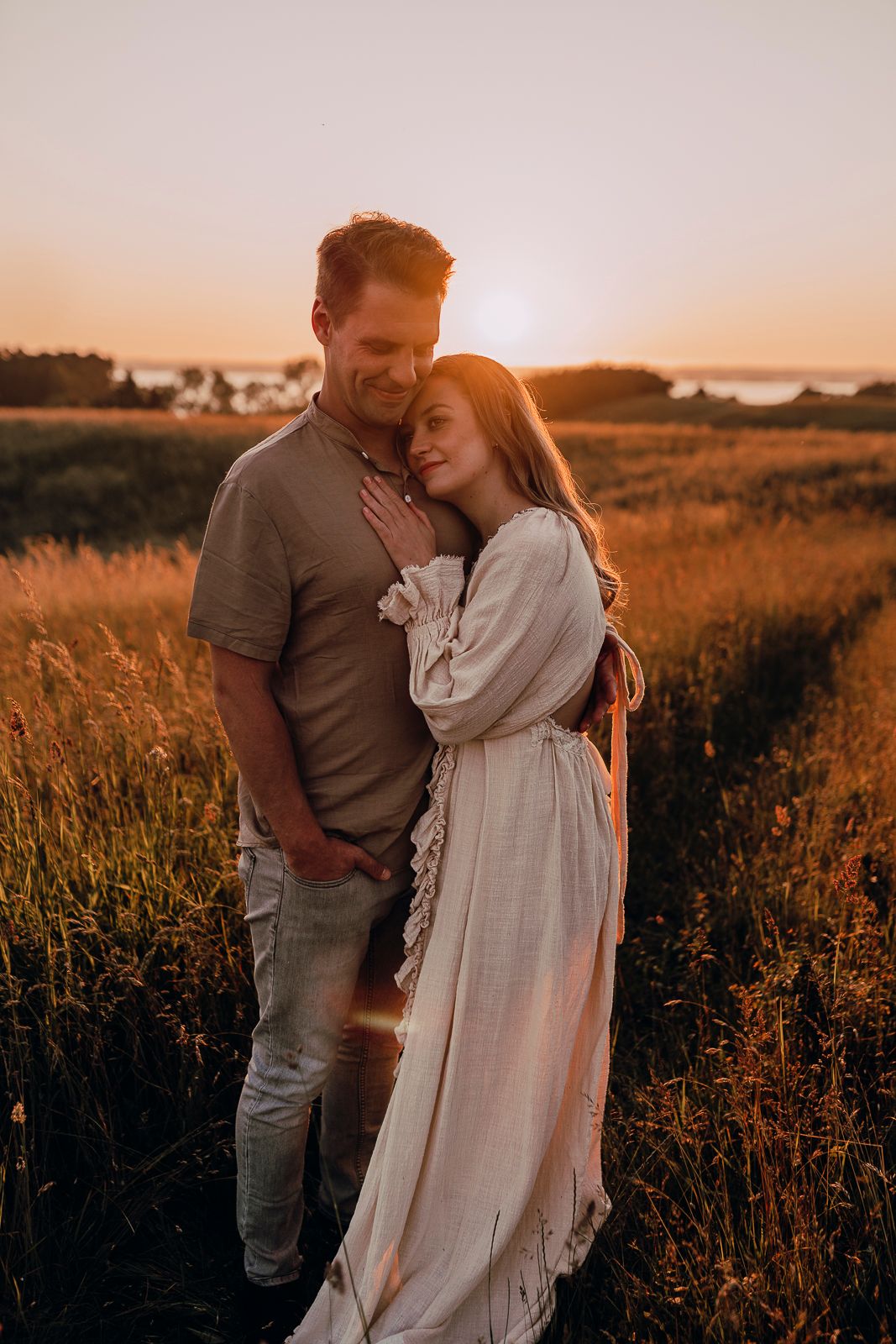 Romantic couple embraces in golden field at sunset with warm lighting creating intimate silhouette against nature backdrop.