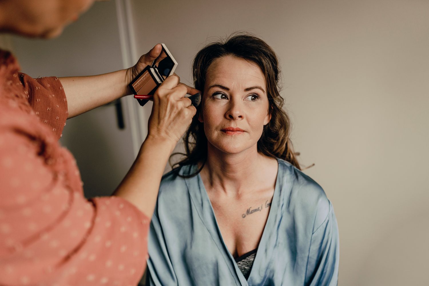 Makeup artist applies cosmetics to model in blue satin robe during professional beauty session.
