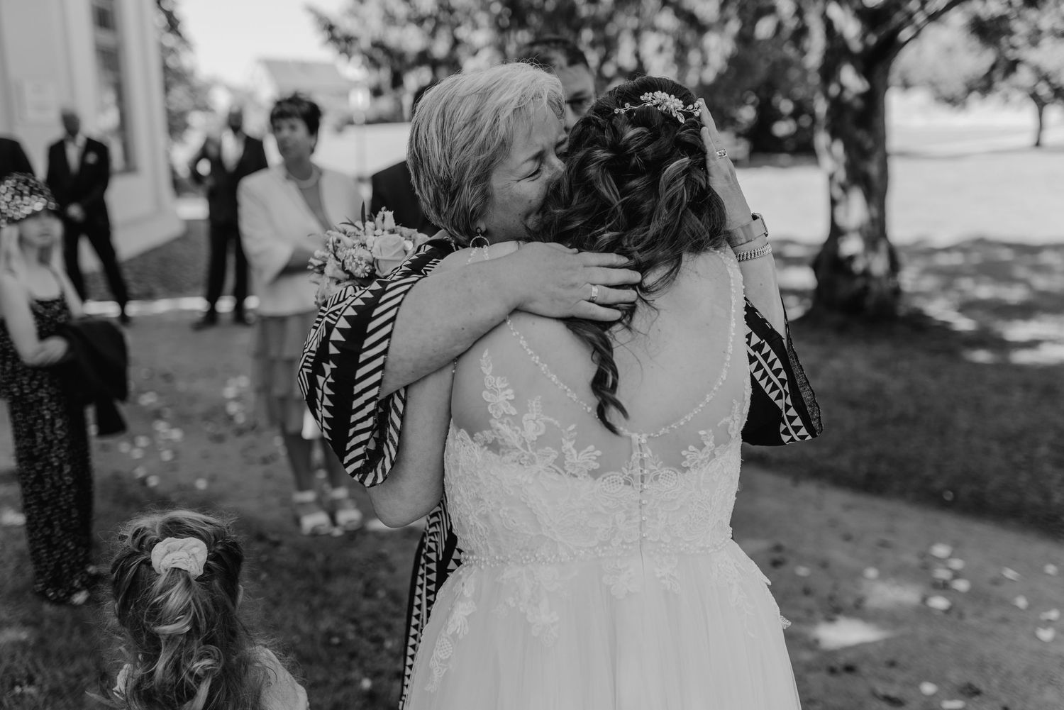 An emotional black and white photograph captures two people embracing outdoors during a wedding celebration.