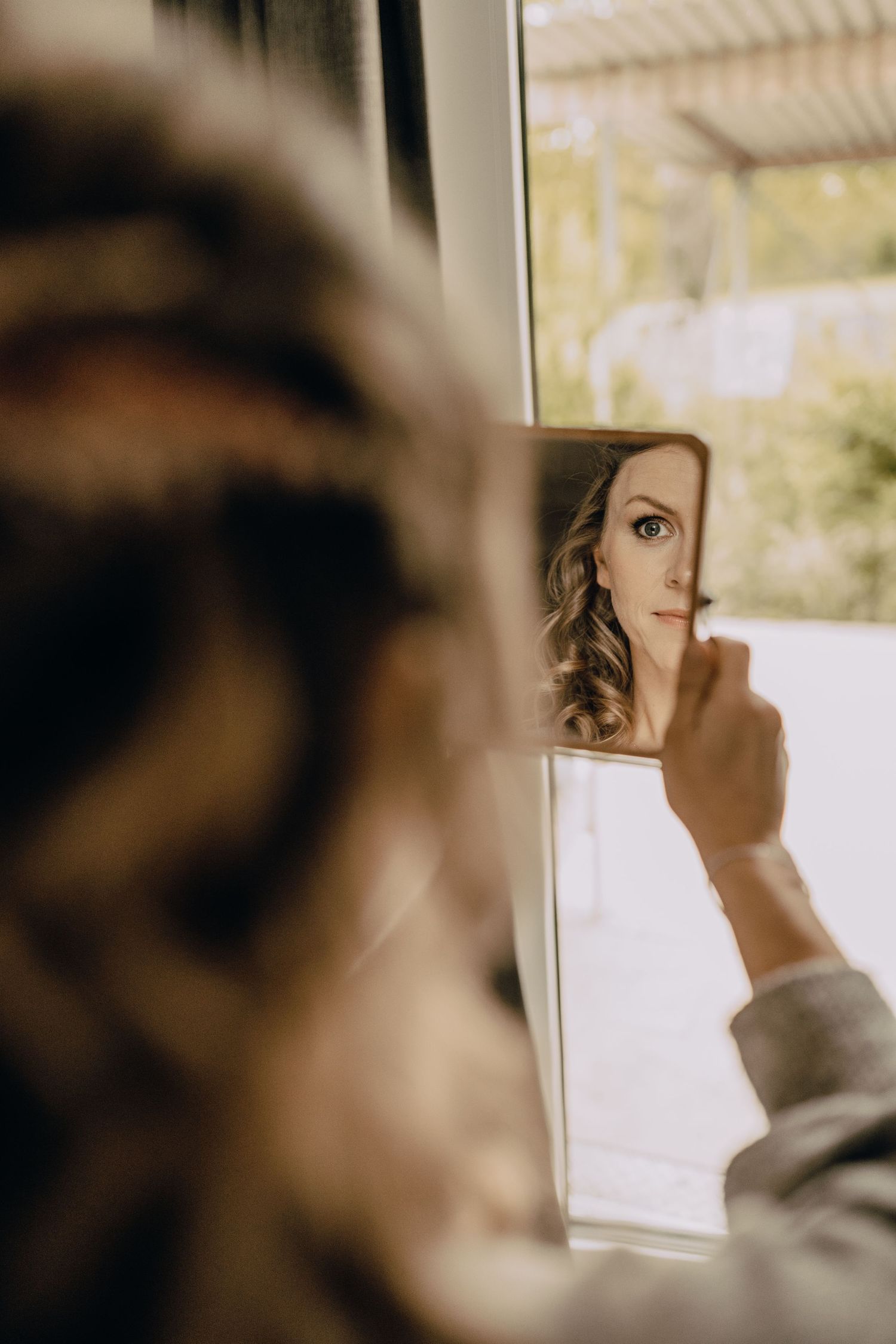 Artistically framed mirror reflection showing half a face with wavy hair and one eye in soft lighting.