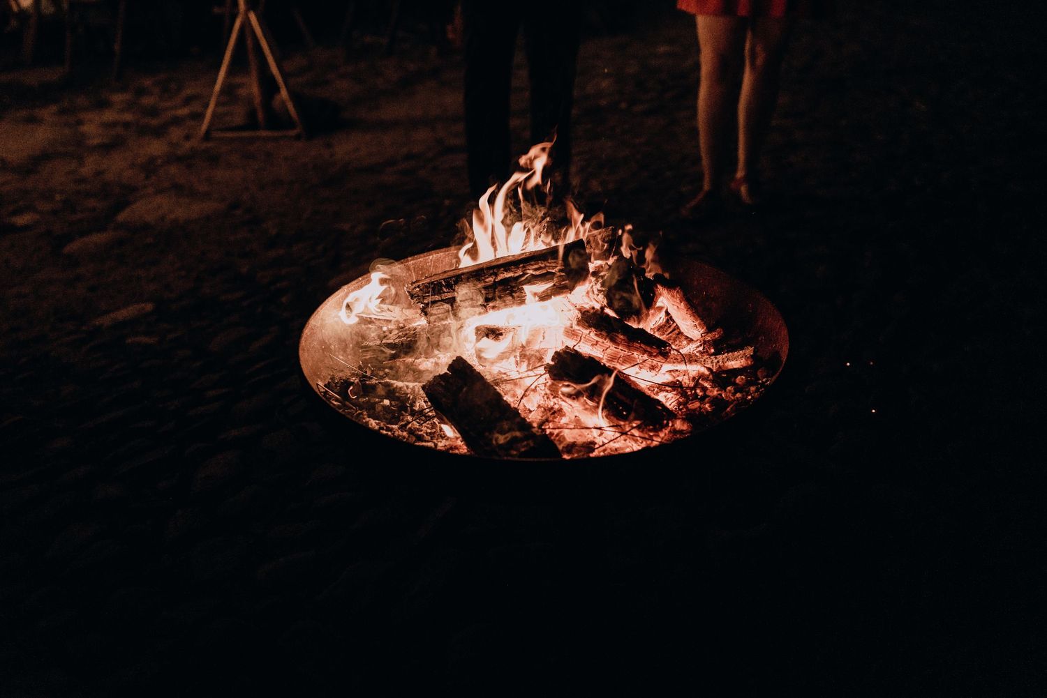 A group of people gather around a glowing bonfire on a dark beach at night.