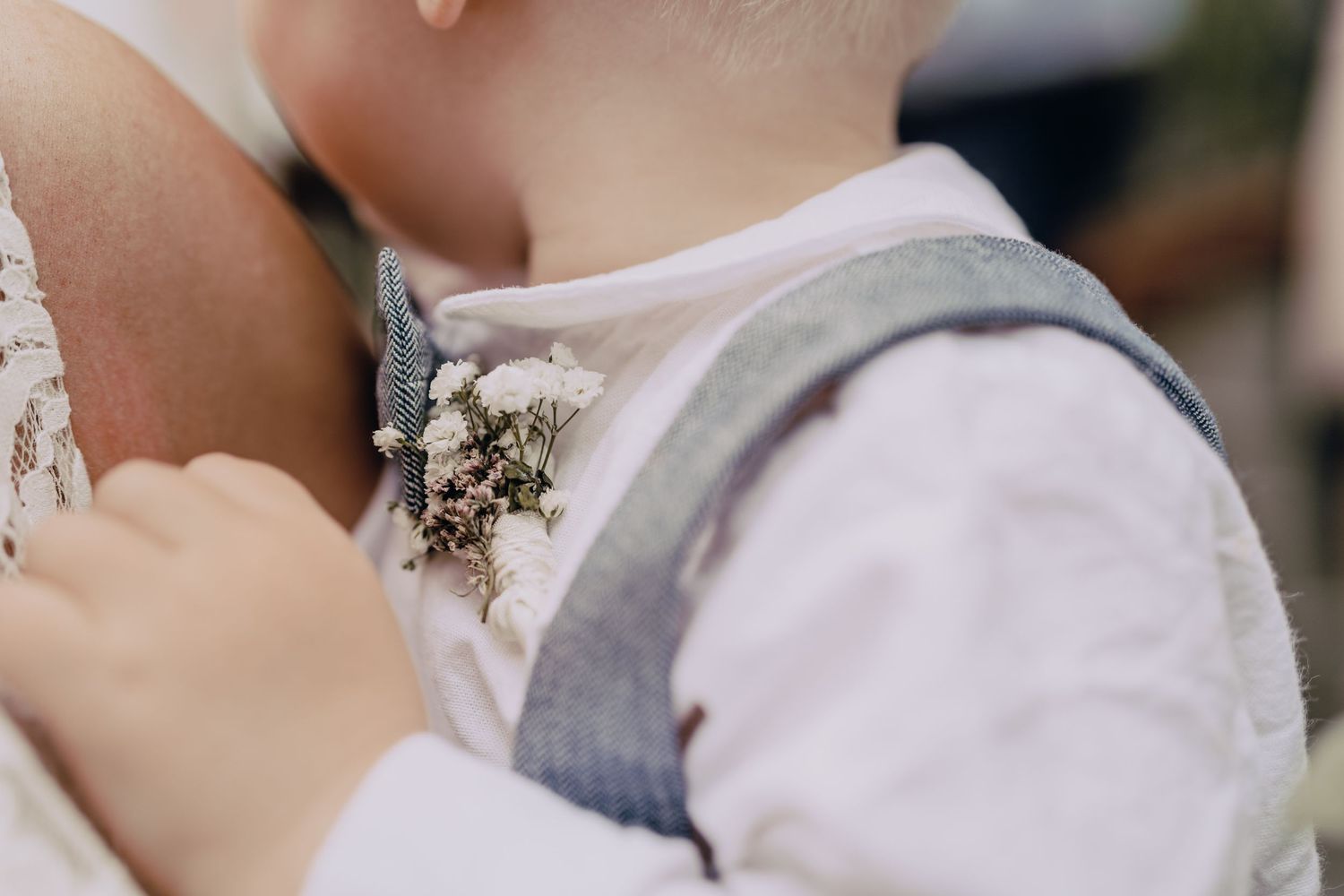 Close-up detail of a baby wearing a formal grey vest with floral boutonniere.