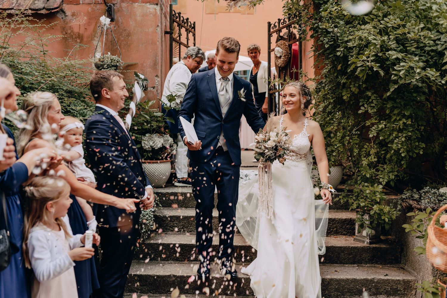 Guests shower newlyweds with confetti as they descend stone steps at outdoor wedding celebration.