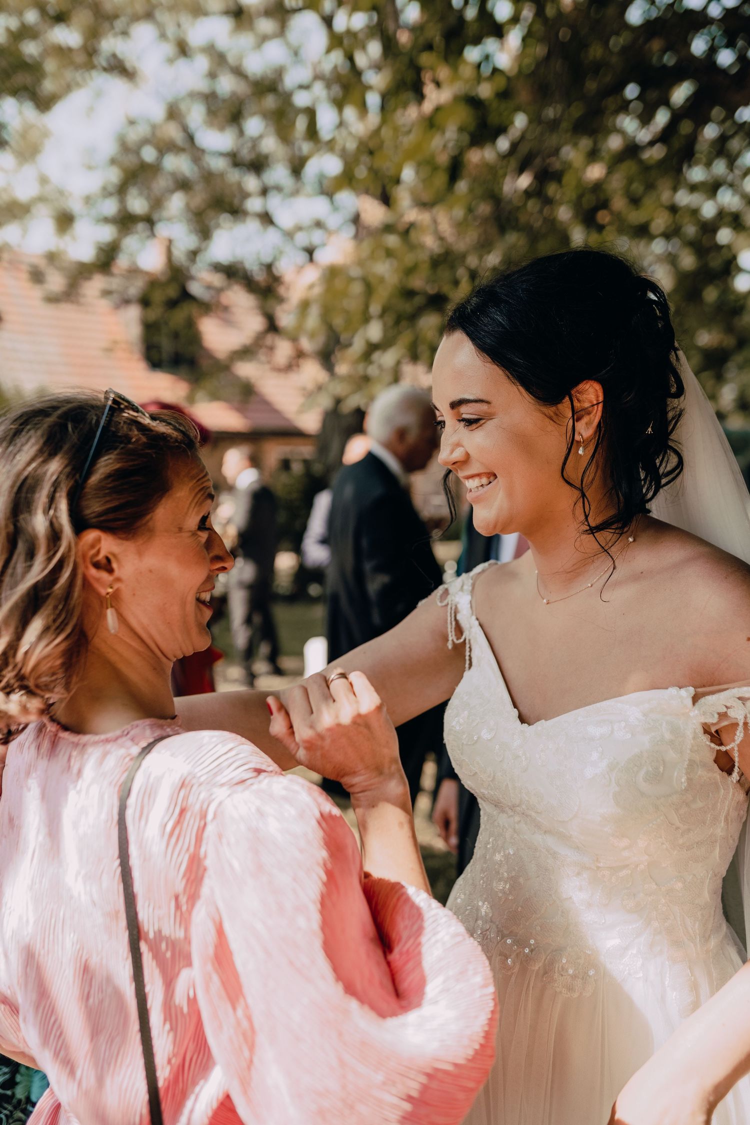 Joyful candid moment between two wedding attendees in outdoor garden setting.