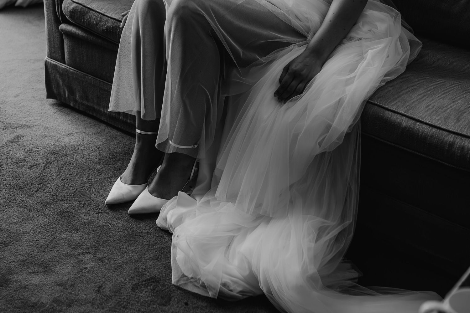 Elegant wedding shoes and flowing white tulle dress photographed in black and white.