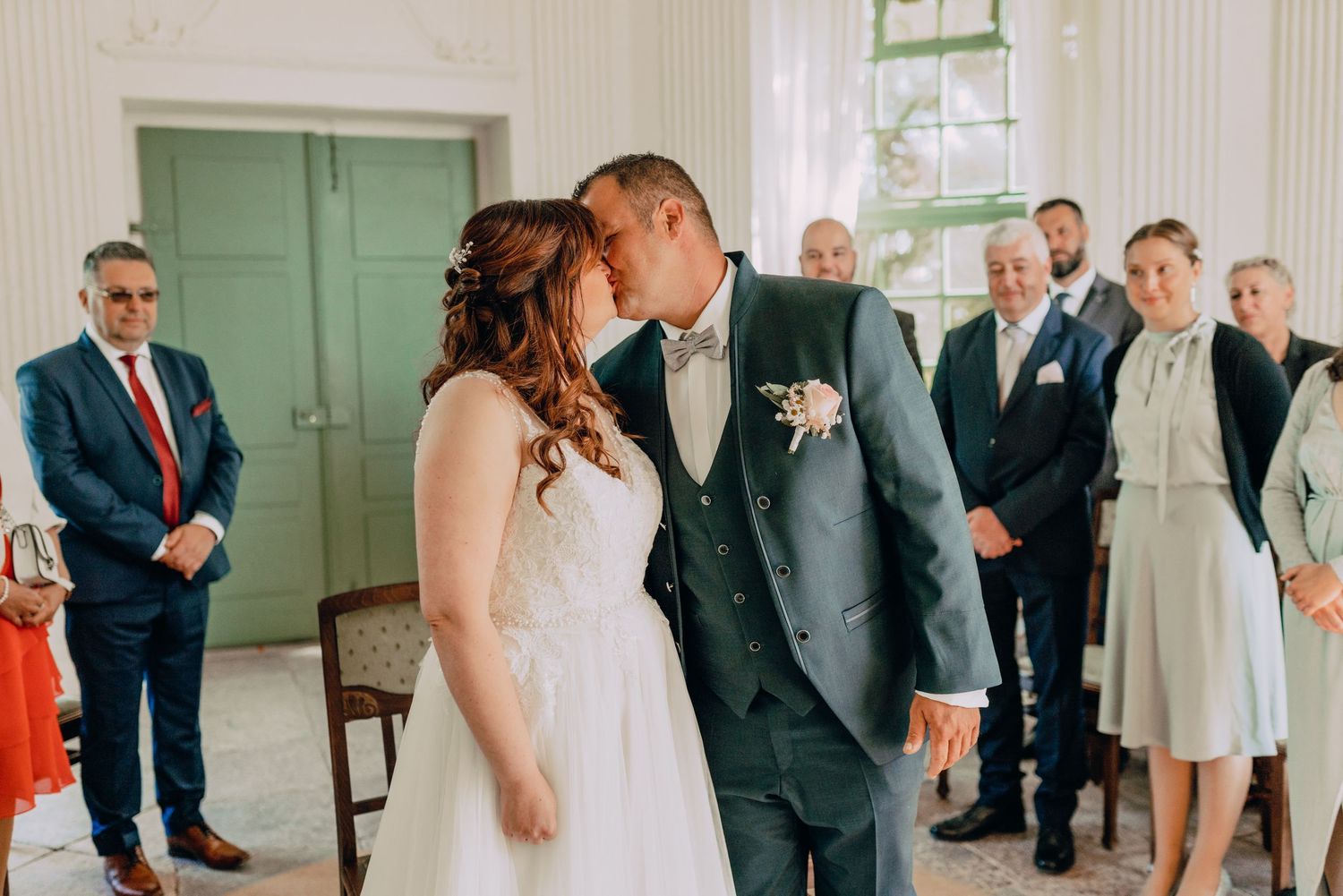 A tender wedding ceremony moment captured in a room with mint green doors and watching guests.