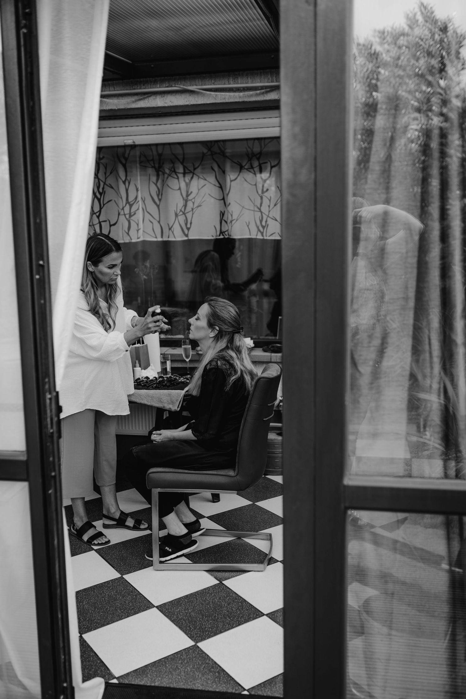 Black and white photo showing a salon interior with checkered floor and two people in a styling session.