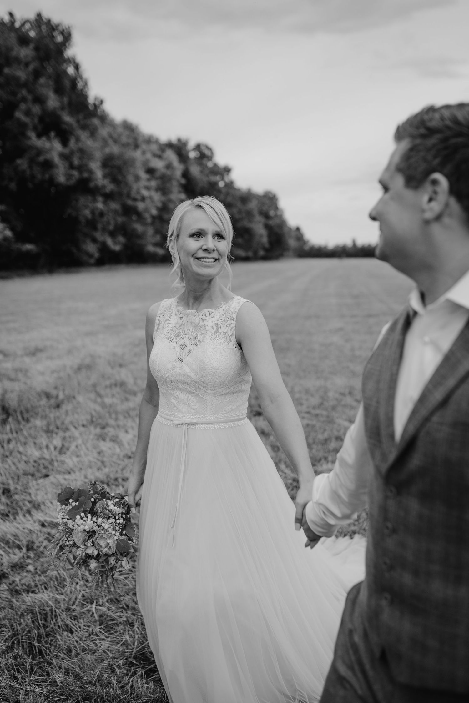 A couple shares a joyful moment together in a sunny meadow wearing wedding attire.