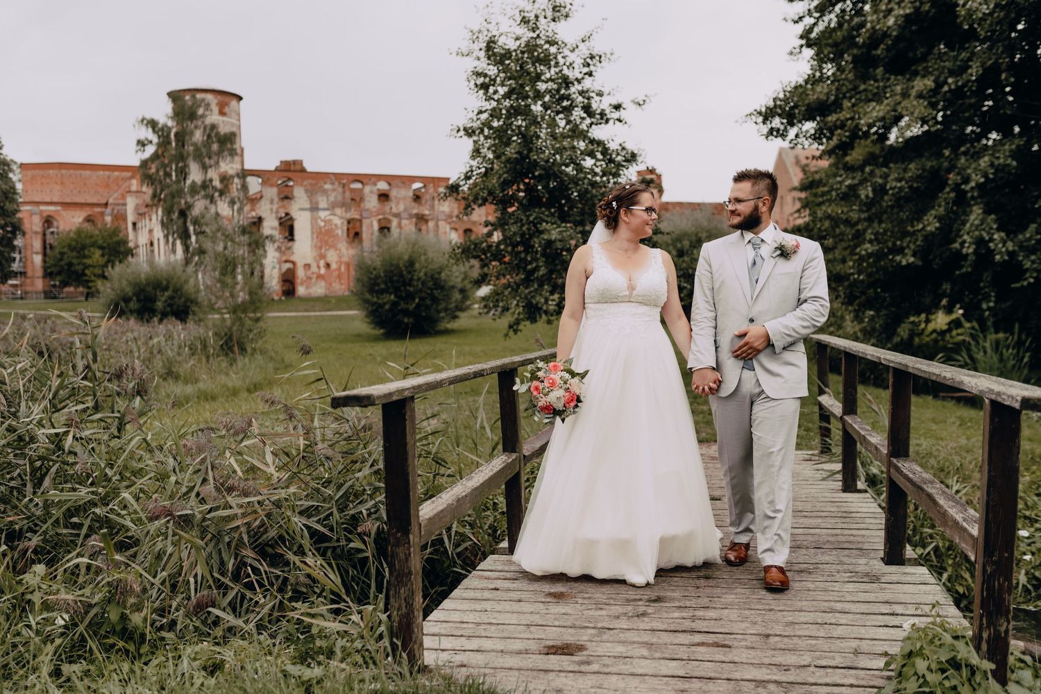 Couple walking on wooden bridge with historic castle building in background.