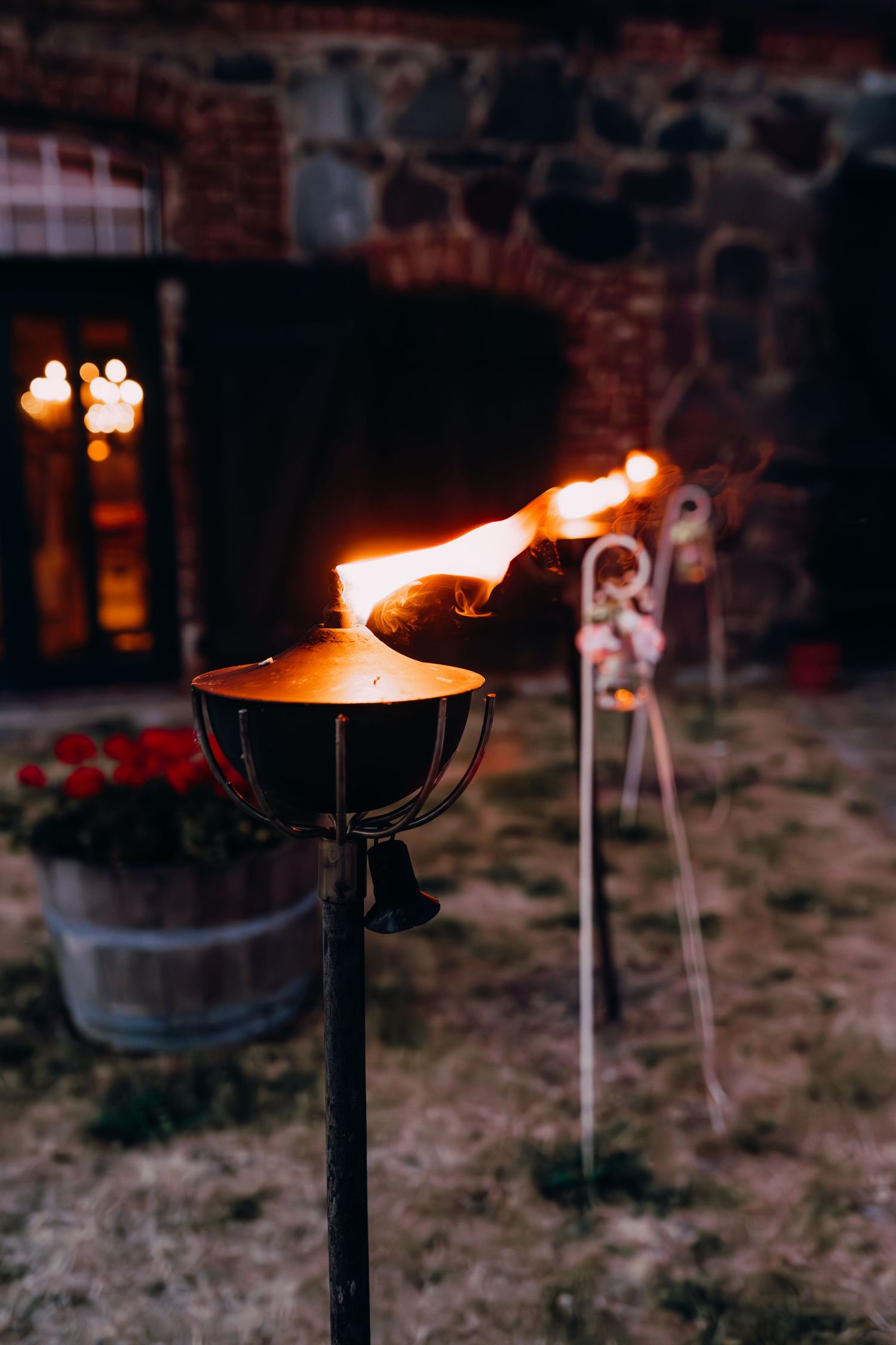 Outdoor tiki torches illuminate a rustic stone wall with warm glowing flames against a dark evening setting.