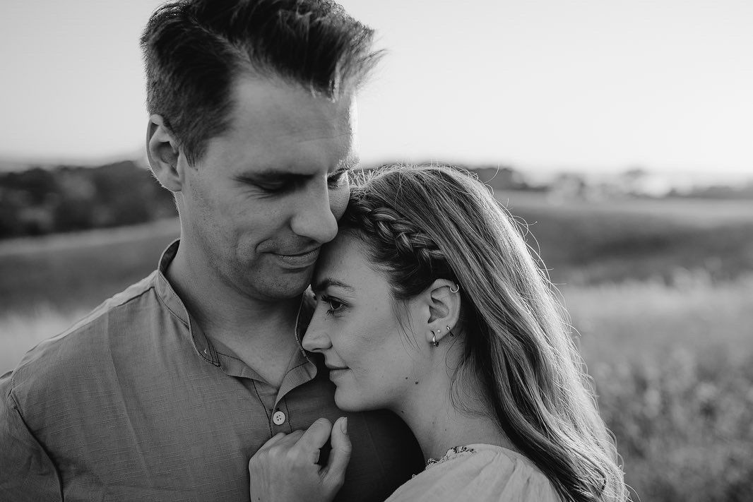 Romantic wedding couple embraces in an outdoor field at sunset during an intimate photo session.