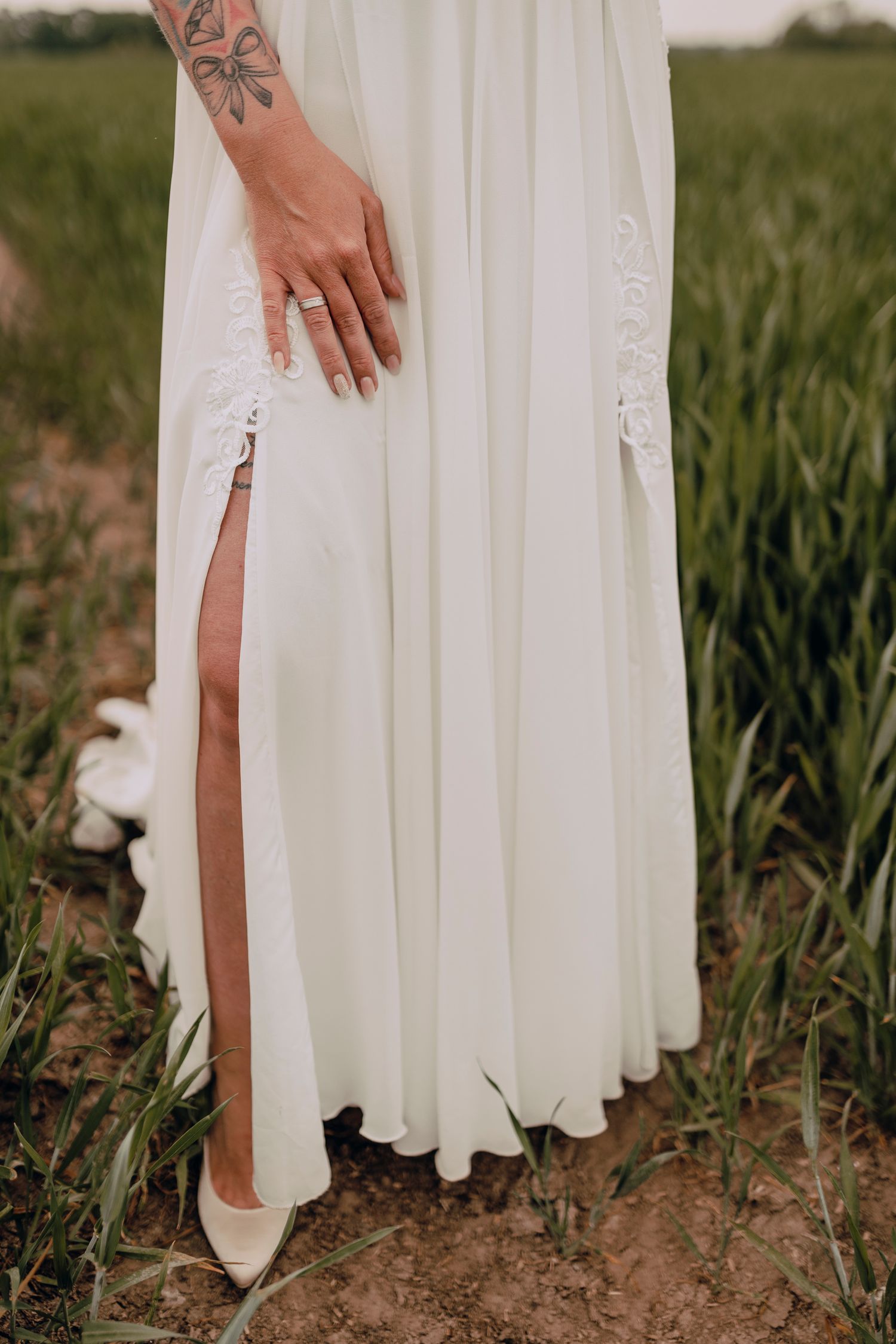 Woman in a flowing white dress walking through a rustic field at sunset, showing only the dress hem and legs.