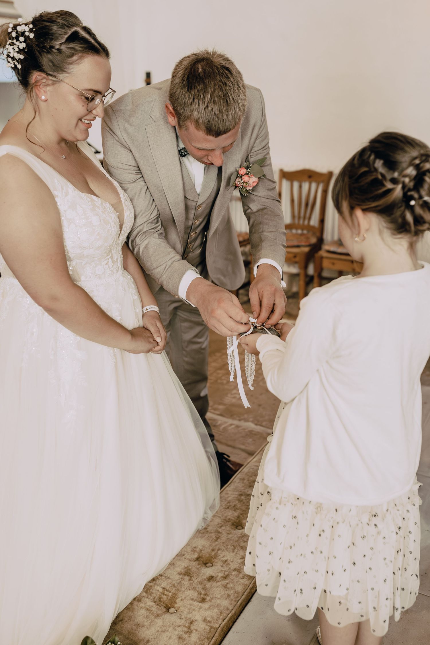 A tender moment is captured during a wedding ceremony as three people gather together near a white wedding dress.